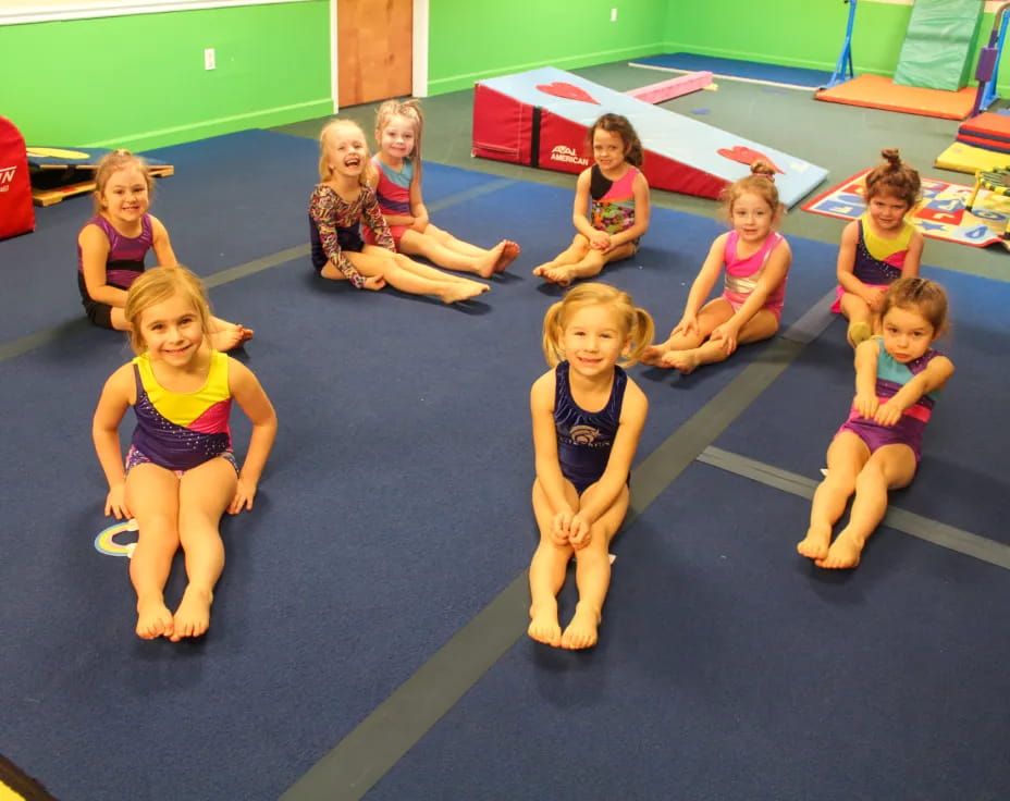 a group of children sitting on a mat in a gym