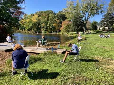 people sitting in chairs on a grass field by a lake