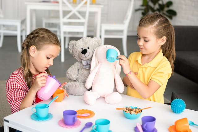 a couple of girls sitting at a table with a teddy bear
