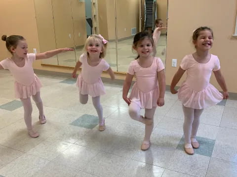 a group of girls wearing pink dresses and dancing in a room