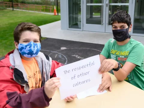 a couple of boys wearing masks and holding a sign