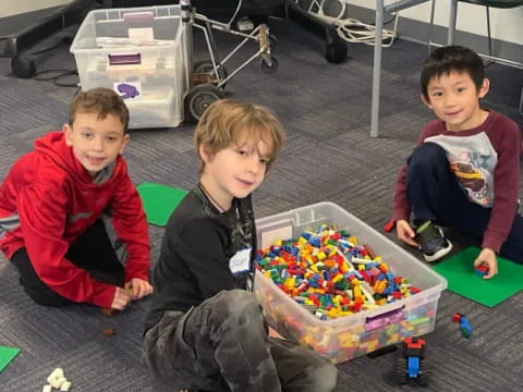 a group of boys sitting on the floor with a large box of toys