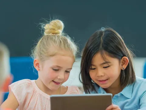 a couple of young girls looking at a laptop