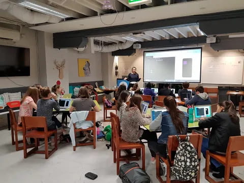 a group of people sitting at desks in a room with a projector screen