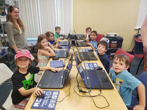 a group of children sitting at a table with laptops