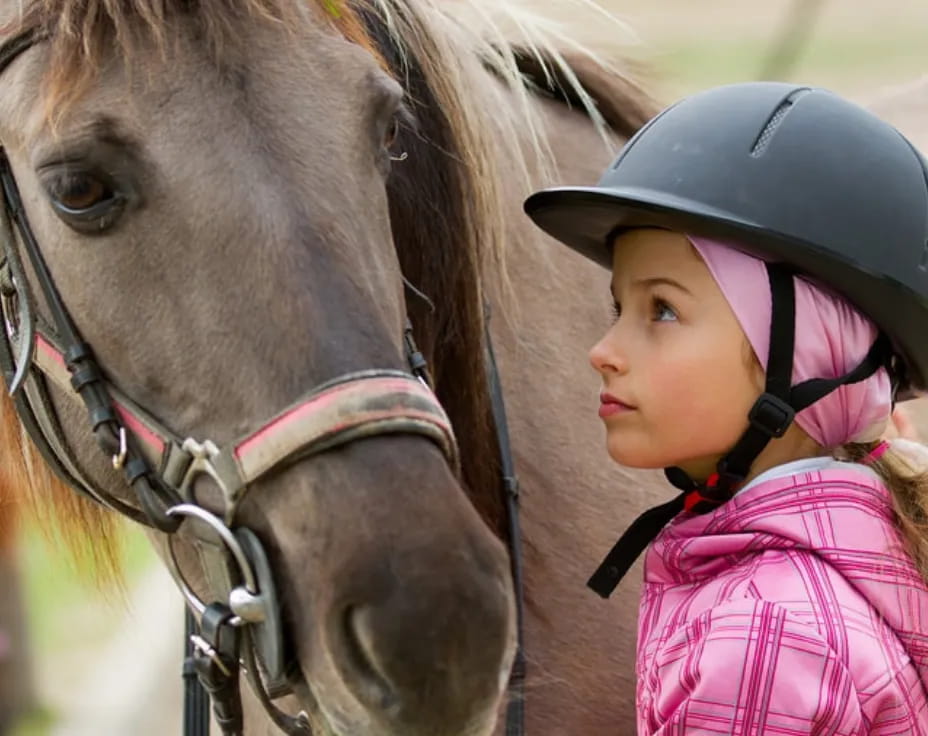 a girl wearing a helmet and riding a horse