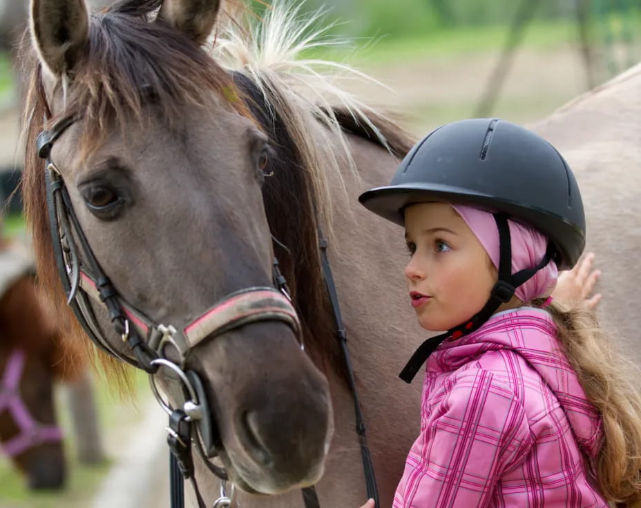 a girl with a helmet standing next to a horse