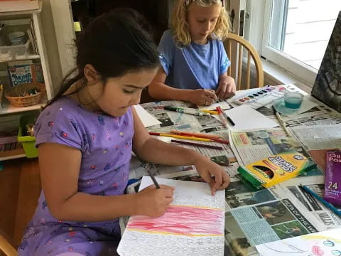 a couple of young girls sitting at a table with books and papers