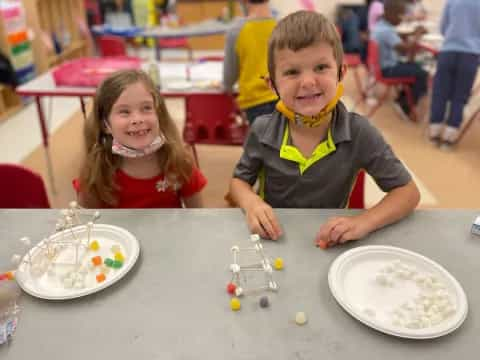 a boy and girl sitting at a table with food and toys