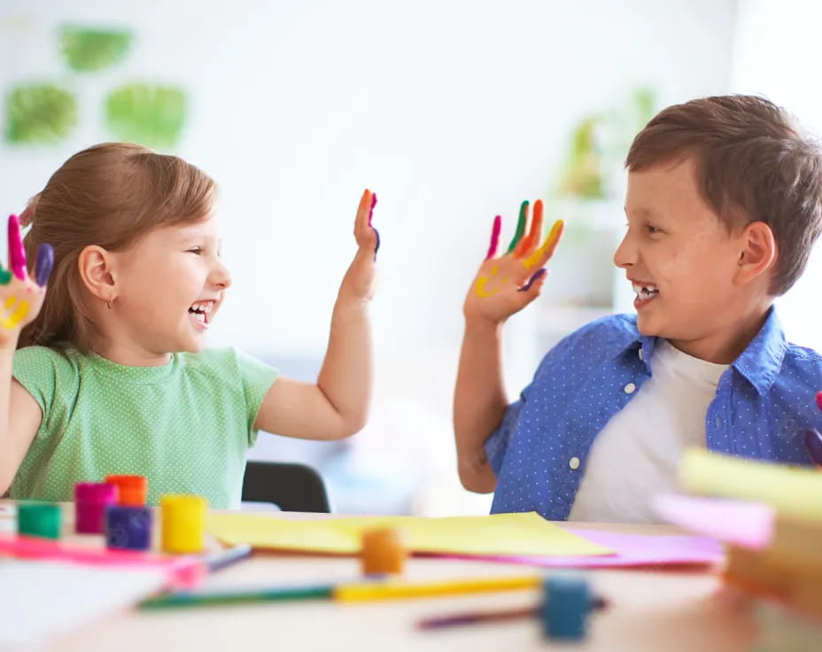 a boy and girl sitting at a table with colored pencils