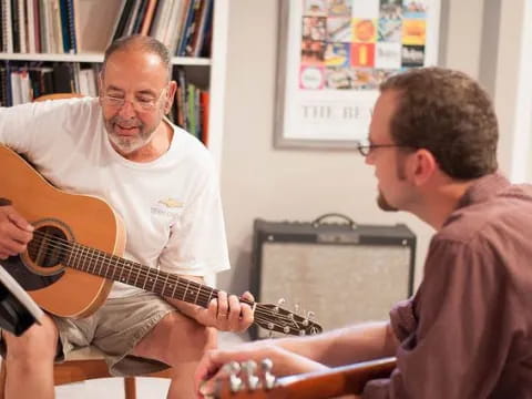 a man playing a guitar next to a man sitting in a chair