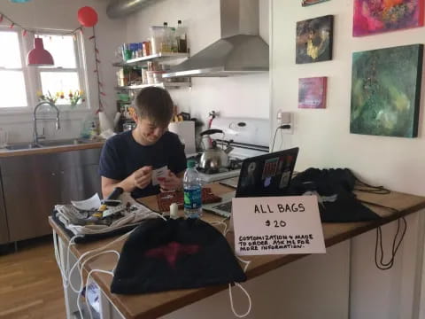 a boy sitting at a table with a laptop and a sign