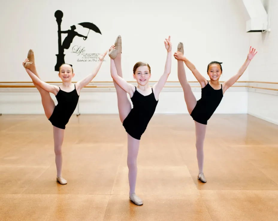 a group of girls in black ballet outfits on a wooden floor