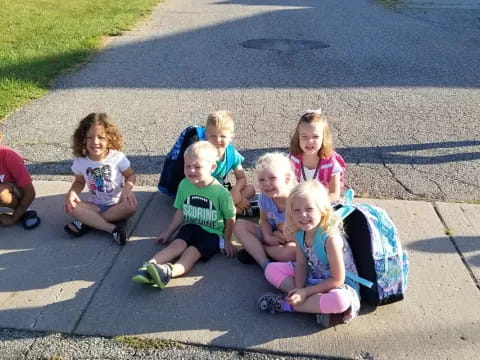 a group of children sitting on a sidewalk