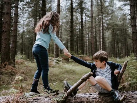a person and a boy playing on a log in the woods