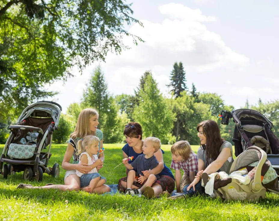 a group of people sitting on the grass with strollers and strollers