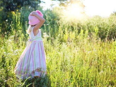 a girl in a dress standing in a field of tall grass