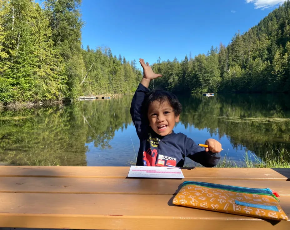 a boy sitting on a dock by a lake with a book and a book