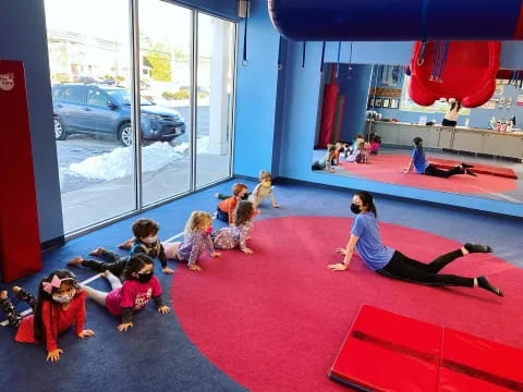 a group of children on a red mat in a room with a red carpet and a window