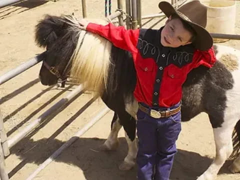 a child wearing a hat and standing next to a horse