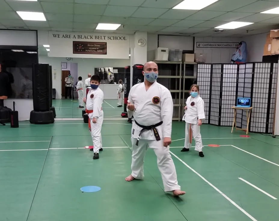 a group of people in white karate uniforms in a room with a green floor and a green mat