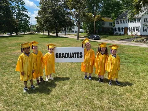 a group of children in yellow graduation gowns holding a sign