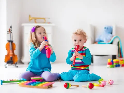 a couple of kids sitting on the floor with toys and a guitar