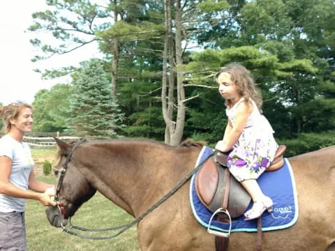 a girl riding a horse with a girl standing by her