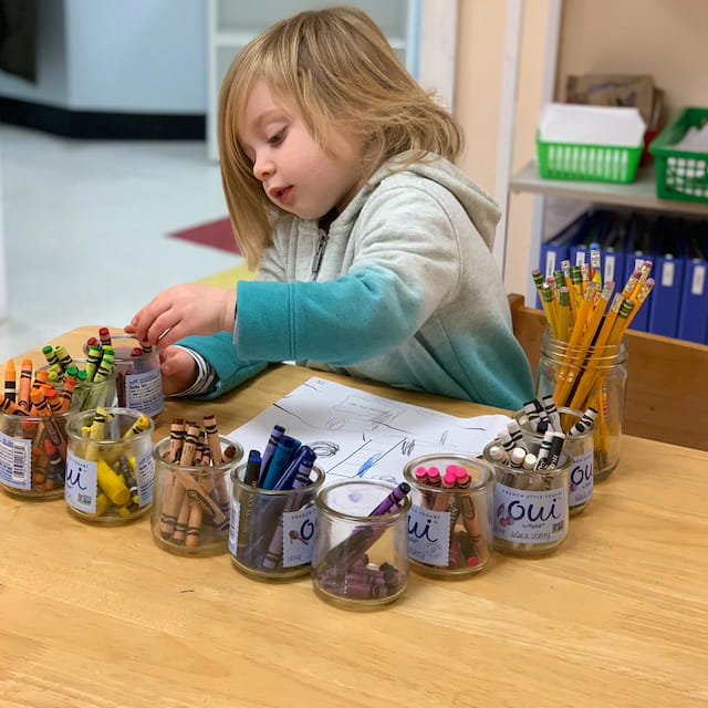 a girl sitting at a table with many jars of jams