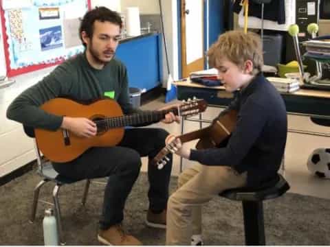 a man playing a guitar next to a boy sitting on a stool
