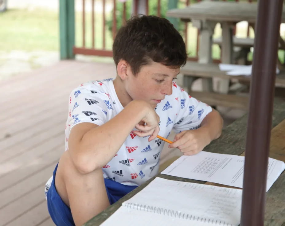 a young man sitting at a table writing on a piece of paper