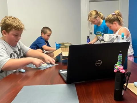 a group of kids sitting at a table looking at a laptop