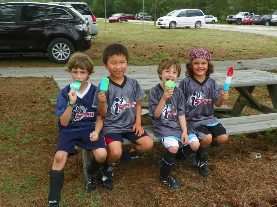 a group of kids sitting on a bench with green cups in their hands