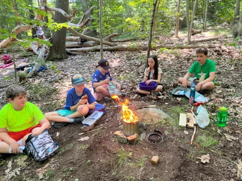 a group of people sitting around a fire in the woods