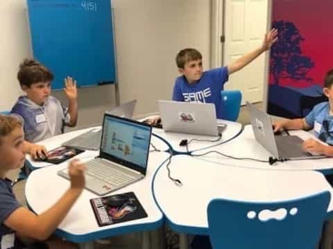 a group of boys sitting at a table with laptops