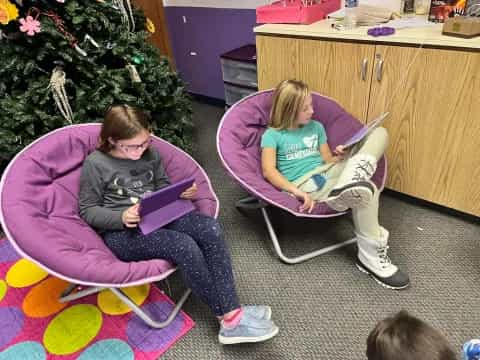 a couple of girls sitting on a purple couch with a laptop