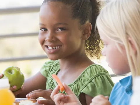 a young girl holding a carrot and a young girl smiling