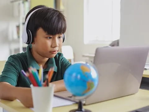 a boy wearing headphones and sitting at a desk with a computer