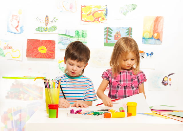a boy and girl sitting at a table with colorful markers