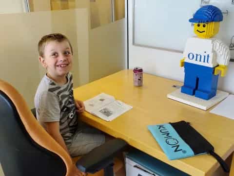 a boy sitting at a desk with a toy robot