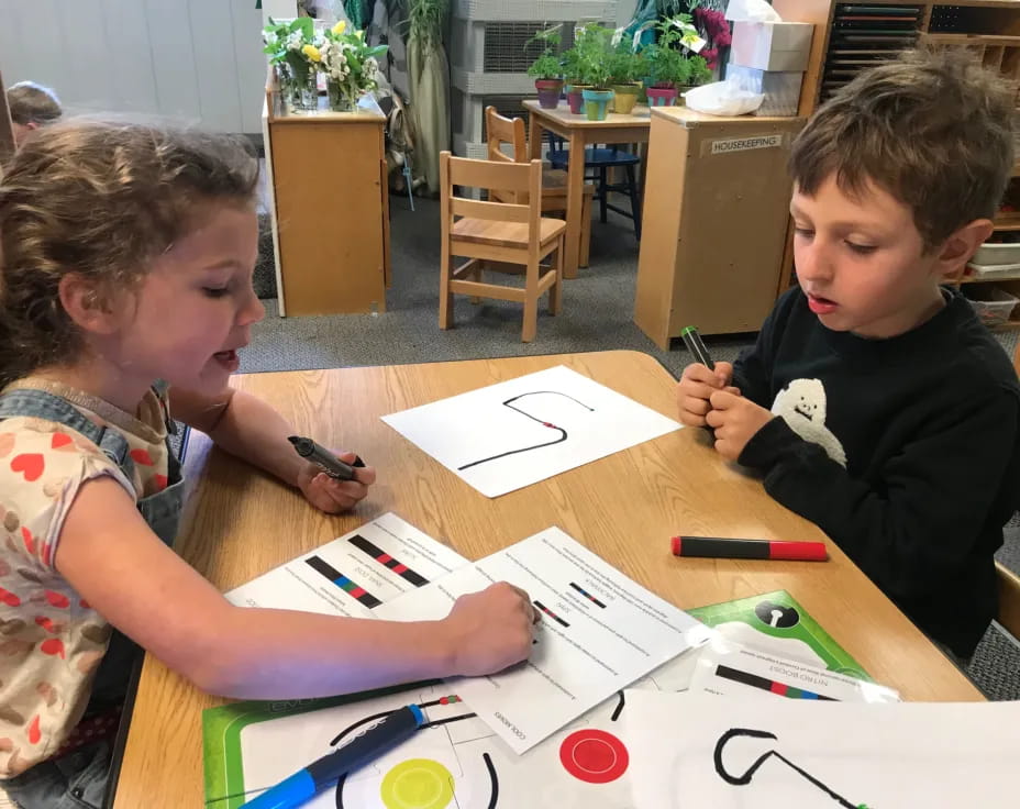 a couple of kids sitting at a table with papers and pens