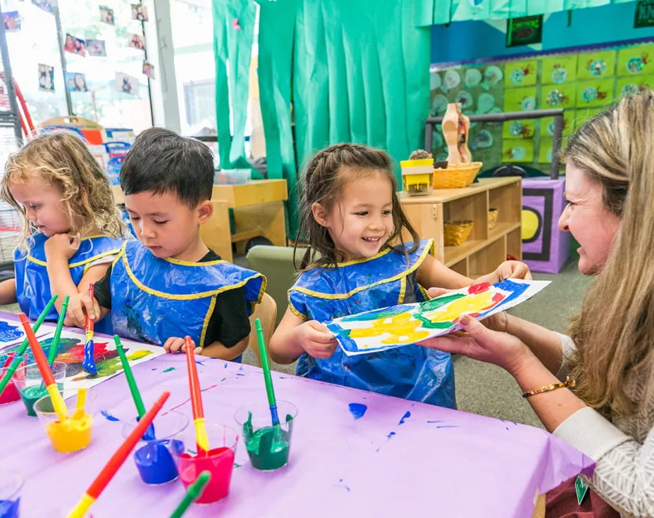 a person and kids sitting at a table with colored markers