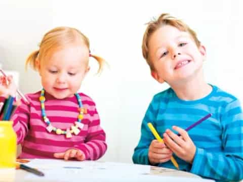 a couple of children sitting at a table with pencils and pens