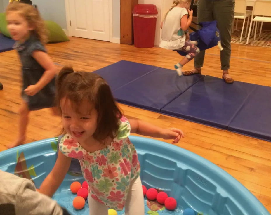 a group of children playing on a mat in a room with a woman standing and a man in