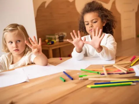 a couple of children sitting at a table with their hands up