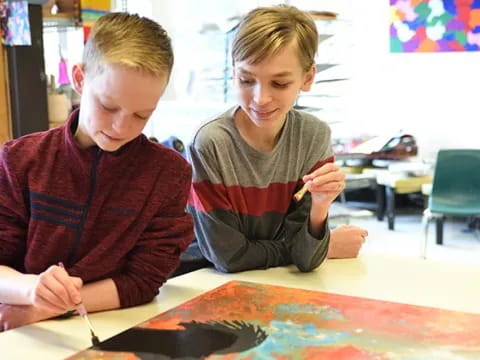 a couple of kids sitting at a table writing on paper