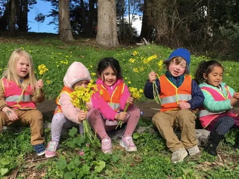 a group of children sitting in a grassy area with flowers