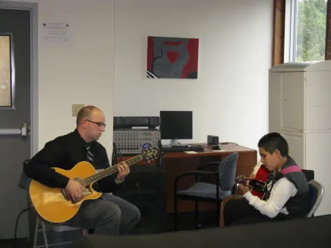 a man playing a guitar next to a boy sitting at a desk