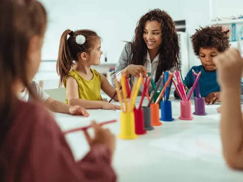 a group of children sitting at a table with colored pencils