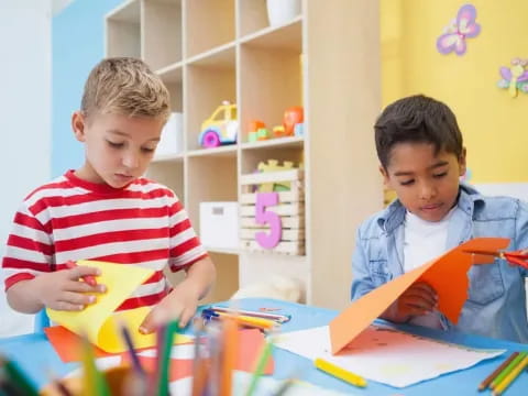 a couple of boys sitting at a table with a book and pencils